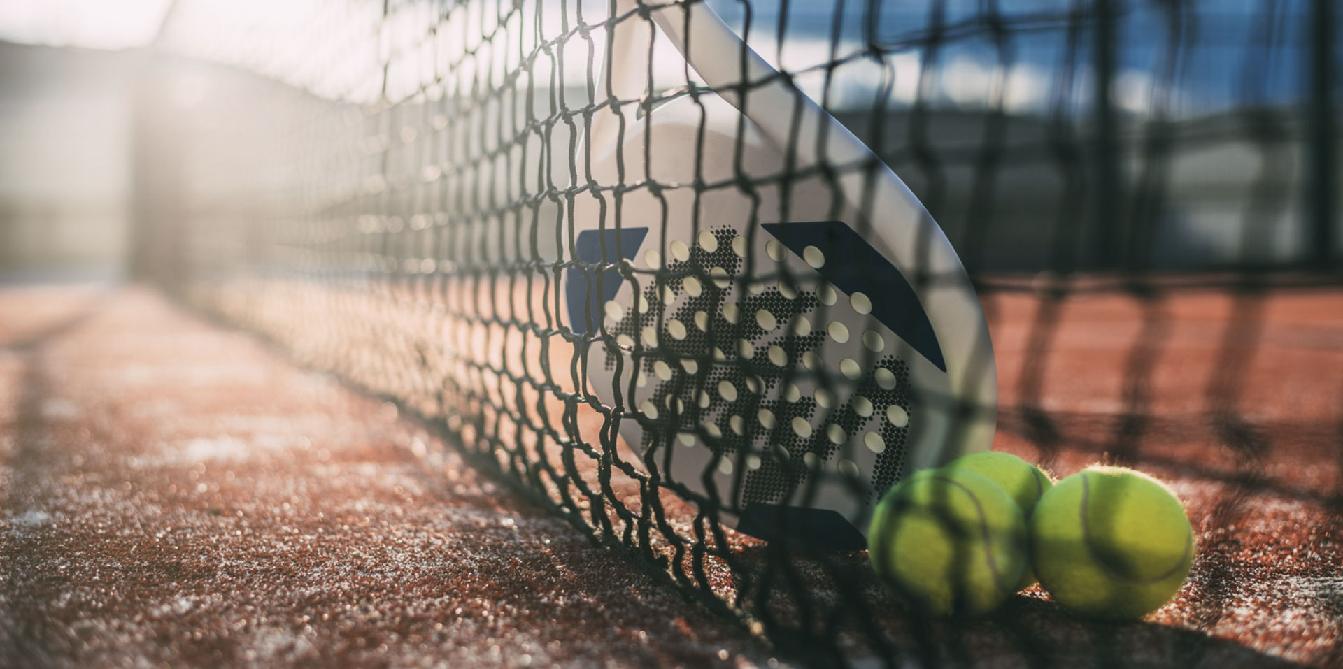Padel racket leaning against net with tennis balls
